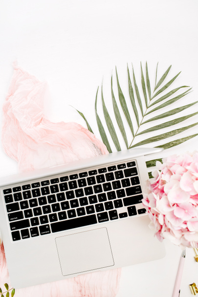 Feminine home office desk with laptop, pink hydrangea flowers bouquet, pastel blanket, monstera leaf plate and accessories on white background. Flat lay, top view workspace. - Photo, Image