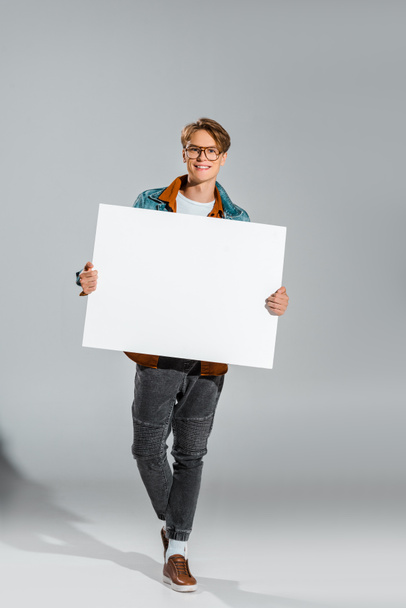 happy handsome hipster holding empty board on grey - Fotoğraf, Görsel