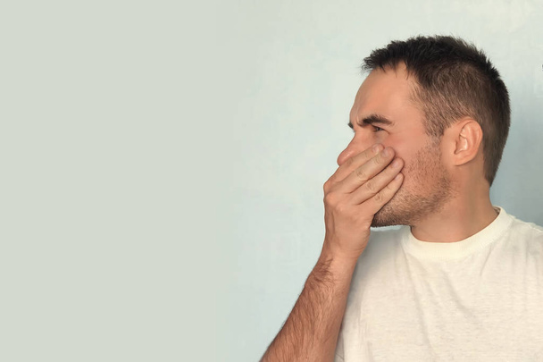 L'homme caucasien pince le nez avec les doigts et regarde avec dégoût à cause de la mauvaise odeur sur fond bleu. Réaction négative du langage corporel à l'expression du visage humain
. - Photo, image