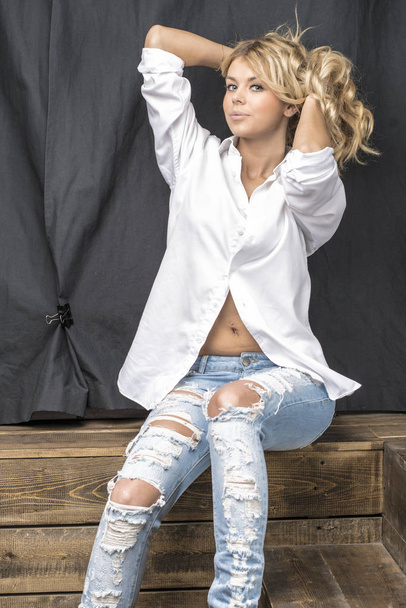 Young beautiful girl blonde in a white shirt and jeans with gaps - Fotografie, Obrázek