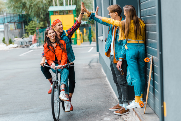 stylish couple riding bicycle and giving highfive to friends on street - Photo, Image