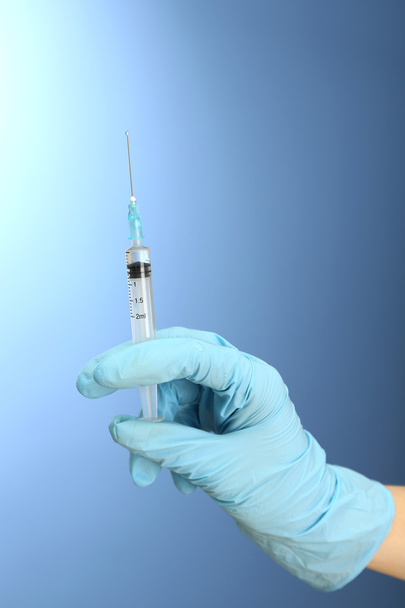 Doctor holding syringe with a vaccine, on blue background - Фото, зображення