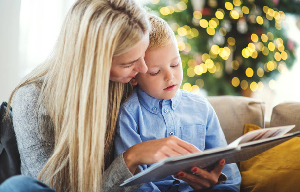 Äiti ja pieni poika istuvat sohvalla kotona jouluna, lukevat kirjaa
. - Valokuva, kuva