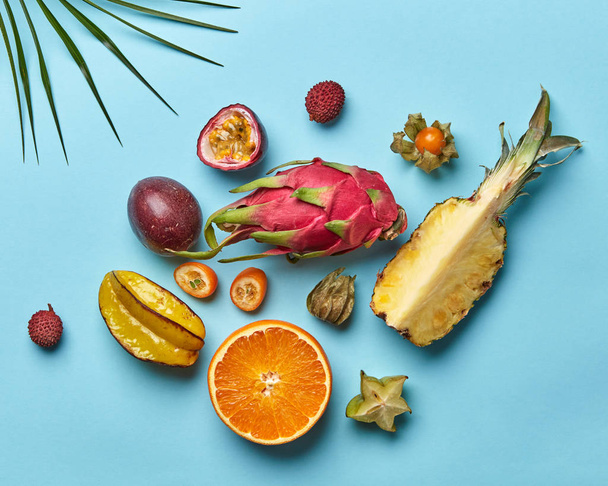 A set of halves of orange, pineapple passion fruit and whole carambola, pitahaya fruit on a blue background decorated with palm leaf from copy space. Flat lay - Фото, зображення