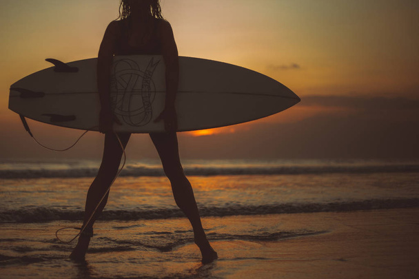 cropped image of woman holding surfboard in sea water and enjoying sunset view  - Fotoğraf, Görsel