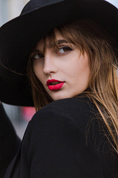 Retrato de rua de uma jovem luxuosa com lábios reg usando chapéu preto e jaqueta
 - Foto, Imagem