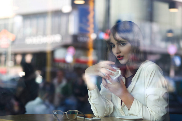 一杯のコーヒーをレストランで過ごす素敵な若い女性。窓からすを通して撮影します。テキストのためのスペース - 写真・画像