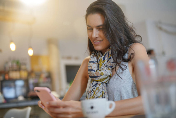 Brunette woman in coffee shop using smartphone - Foto, imagen