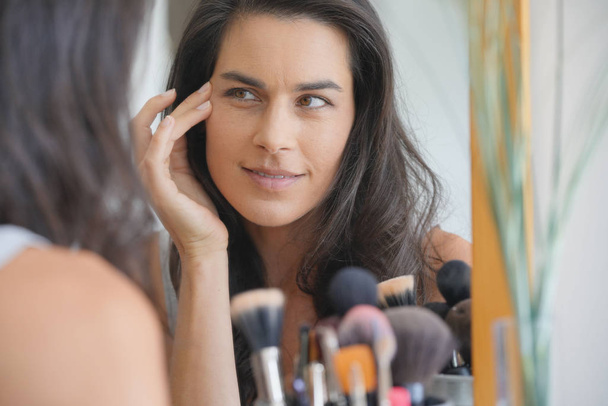 Beautiful woman in front of mirror looking at her face - Fotoğraf, Görsel