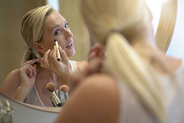 40-year-old woman putting makeup on in front of mirror - Foto, Imagem