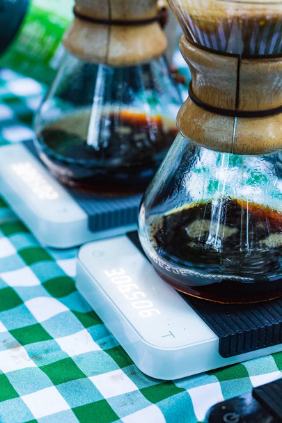 Kaffeetropfen in handwerklich hergestellten Glasbrauern auf elektronischen Waagen übergießen, während sie draußen auf einem Picknicktisch sitzen - Foto, Bild