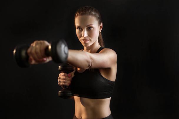 beautiful young girl goes in for sports with dumbbells on a black background - Fotografie, Obrázek