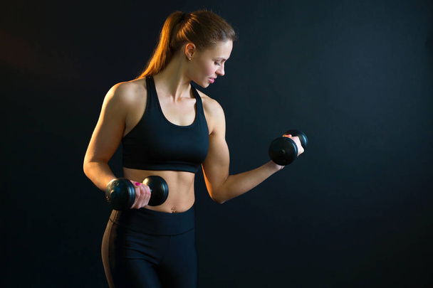 beautiful young girl goes in for sports with dumbbells on a black background - Foto, immagini