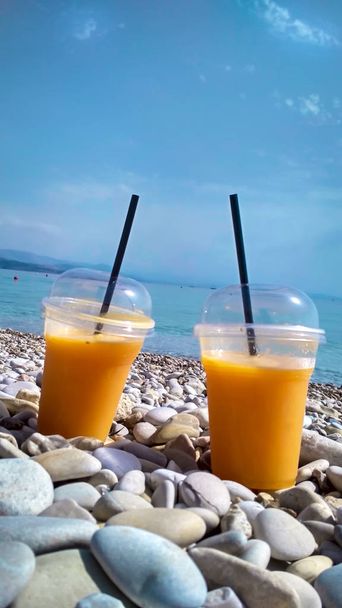 Two glasses of fresh orange juice on pebble beach, day - Foto, imagen
