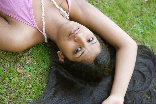 Vista sobre la cabeza de una adolescente india acostada con su pelo oscuro sobre hierba verde
. - Foto, Imagen