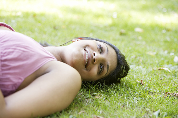 Indischer Teenager legt sich lächelnd auf das grüne Gras im Park. - Foto, Bild
