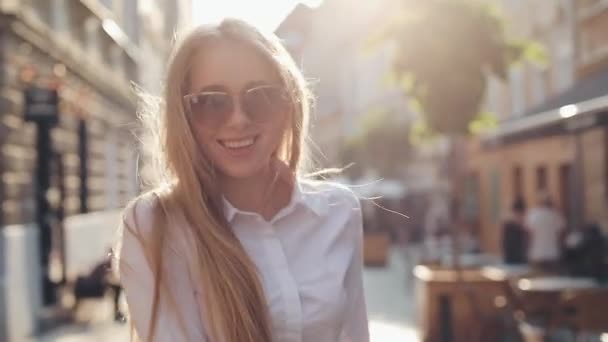 Charming young woman with a magnificent brown hair and stylish sunglasses. Attractive young lady is rushing in the city-center, she turns to camera and smiles - Metraje, vídeo