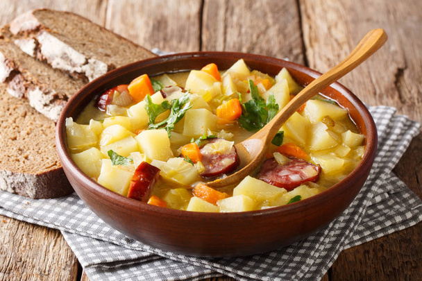 Толстый картофельный суп с сосисками и петрушкой в миске с хлебом крупным планом на столе. hhhonta
 - Фото, изображение