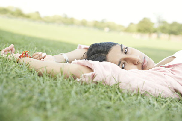 indian girl laying down on green grass looking at camera. - Photo, Image