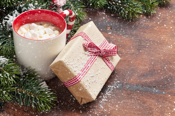 Weihnachtsgeschenkschachtel, Tasse heißer Schokolade mit Eibisch und Tannenzweig bedeckt von Schnee auf Holzgrund. Weihnachtskulisse mit Platz für Ihre Grüße - Foto, Bild