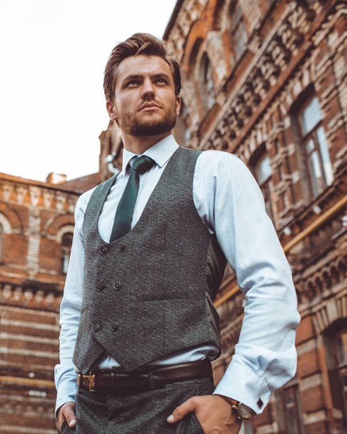 businessman in suit vest posing at brick building, holding hands in pockets  - Fotografie, Obrázek