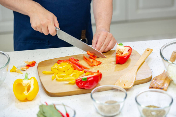 Mens hands cut red and yellow pepper on the wooden board close up - Foto, Imagem