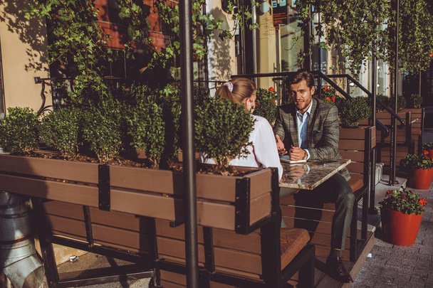 guapo caucásico hombre sentado al aire libre en la cafetería en la reunión con la mujer
  - Foto, imagen
