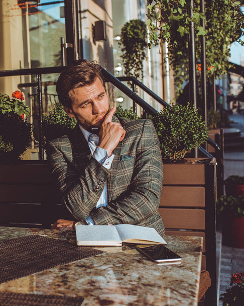 thinking handsome Caucasian man sitting outdoors in cafe at table - 写真・画像