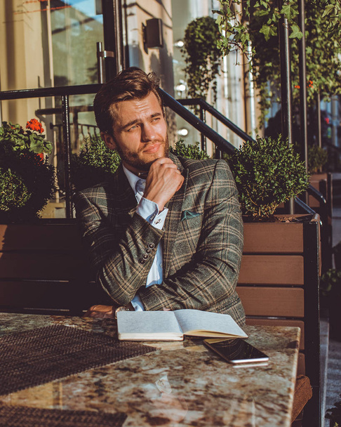 handsome Caucasian man sitting outdoors in cafe at table and posing on camera with hand on chin  - 写真・画像