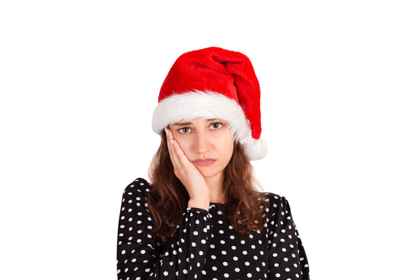 Displeased fed up attractive woman in dress leaning head on palm. sulking from displeasure. emotional girl in santa claus christmas hat isolated on white background. holiday concept. - Photo, Image