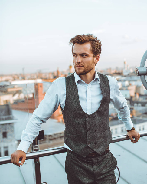 stylish handsome Caucasian man in suit vest standing posing at city view telescope on roof  - Fotoğraf, Görsel