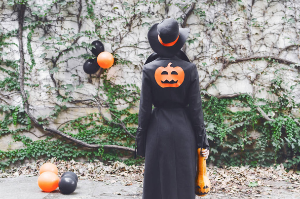 Вид сзади на молодую женщину, стоящую снаружи в костюме Хэллоуина и держащую тыкву
 - Фото, изображение