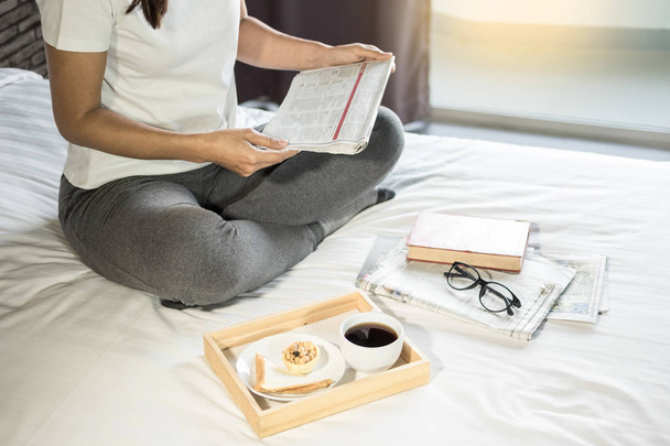 Woman reading book or newspaper and drinking coffee breakfast on bed during the morning - Foto, imagen