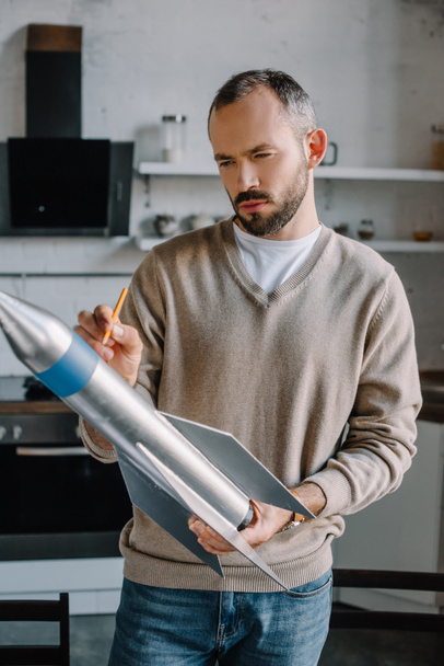 ingeniero guapo mirando el nuevo modelo de cohete en casa
 - Foto, Imagen