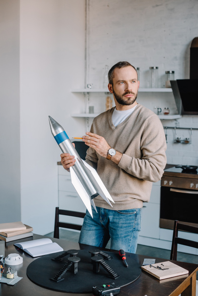 Ingeniero guapo sosteniendo el modelo de cohete en casa y mirando hacia otro lado
 - Foto, imagen