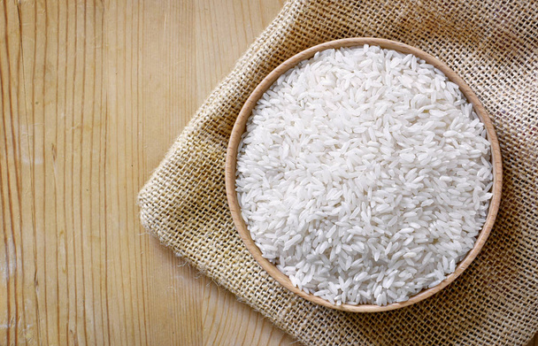 Raw, parboiled rice in a wooden bowl. Rice dish on a wooden table, diet or healthy eating scene. - Photo, Image
