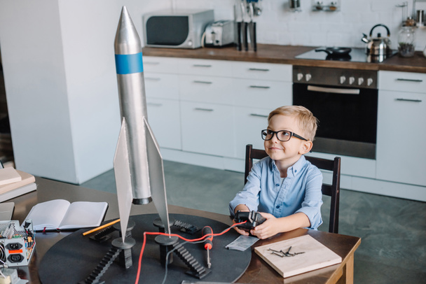adorable chico sentado a la mesa y probar el modelo de cohete en la cocina en fin de semana
 - Foto, imagen