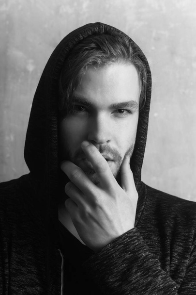 Young man hiding unshaven face with hand wearing grey hoodie - 写真・画像
