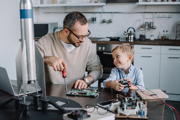 alegre padre e hijo reparación de placa de circuito y mirándose en casa
 - Foto, Imagen