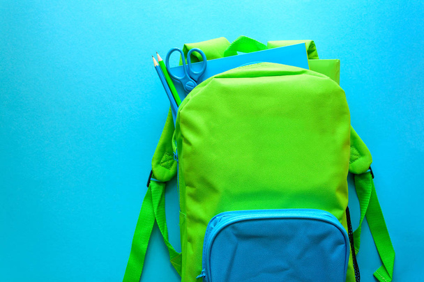 Back to school concept. Green backpack with school supplies on blue background. Top view. Copy space - Foto, Imagen