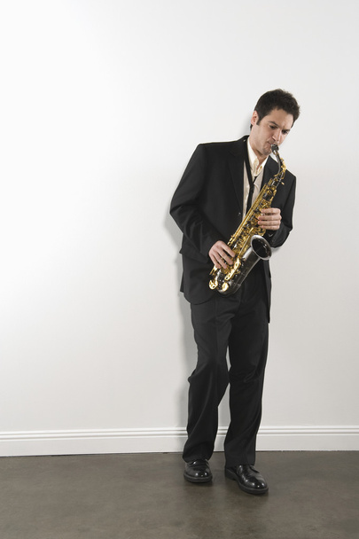 L'homme se tient en costume jouant du saxophone
 - Photo, image