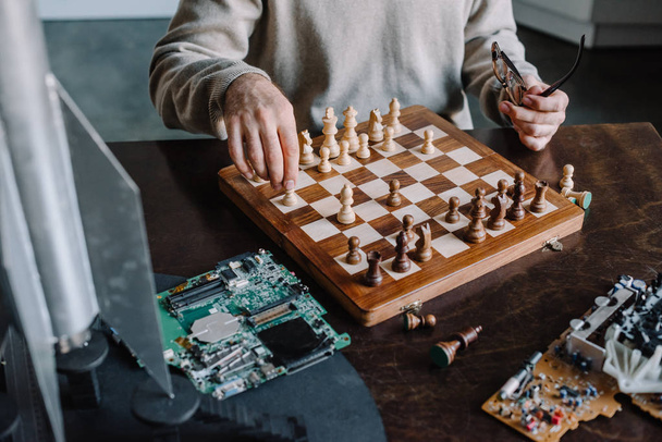 bijgesneden afbeelding van man spelen schaak aan tafel thuis - Foto, afbeelding
