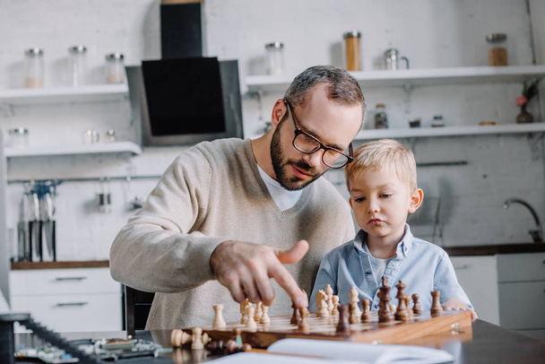 Padre enseñando a su hijo a jugar ajedrez en casa
 - Foto, Imagen