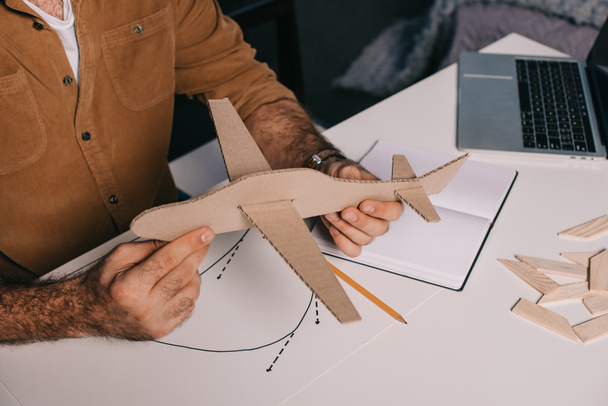 cropped shot of man holding cardboard plane model while modeling at home - Foto, immagini