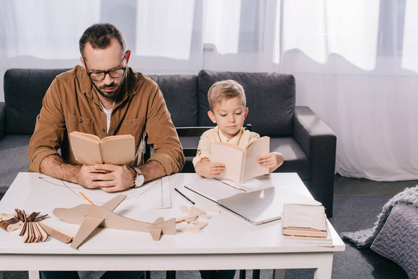 high angle view of father and little son reading books while modeling plane at home - Фото, изображение