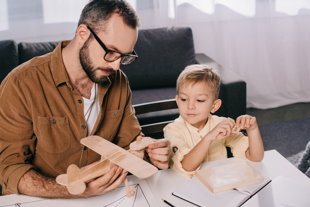 Aus der Vogelperspektive: Vater und kleiner Sohn modellieren gemeinsam Spielzeugflugzeug zu Hause - Foto, Bild