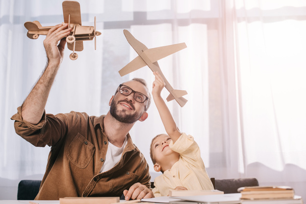glücklicher Vater und kleiner Sohn spielen zu Hause mit Holzflugzeugmodellen - Foto, Bild