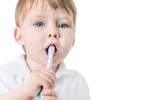 Cute blue-eyed blond boy in a white polo shirt brushing his teeth with a toothbrush. Isolated - Foto, immagini