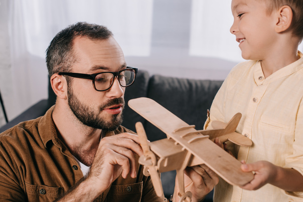 close-up view of father and son playing with wooden toy plane at home - Φωτογραφία, εικόνα