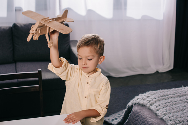 high angle view of adorable child playing with wooden plane model at home - Foto, Imagen